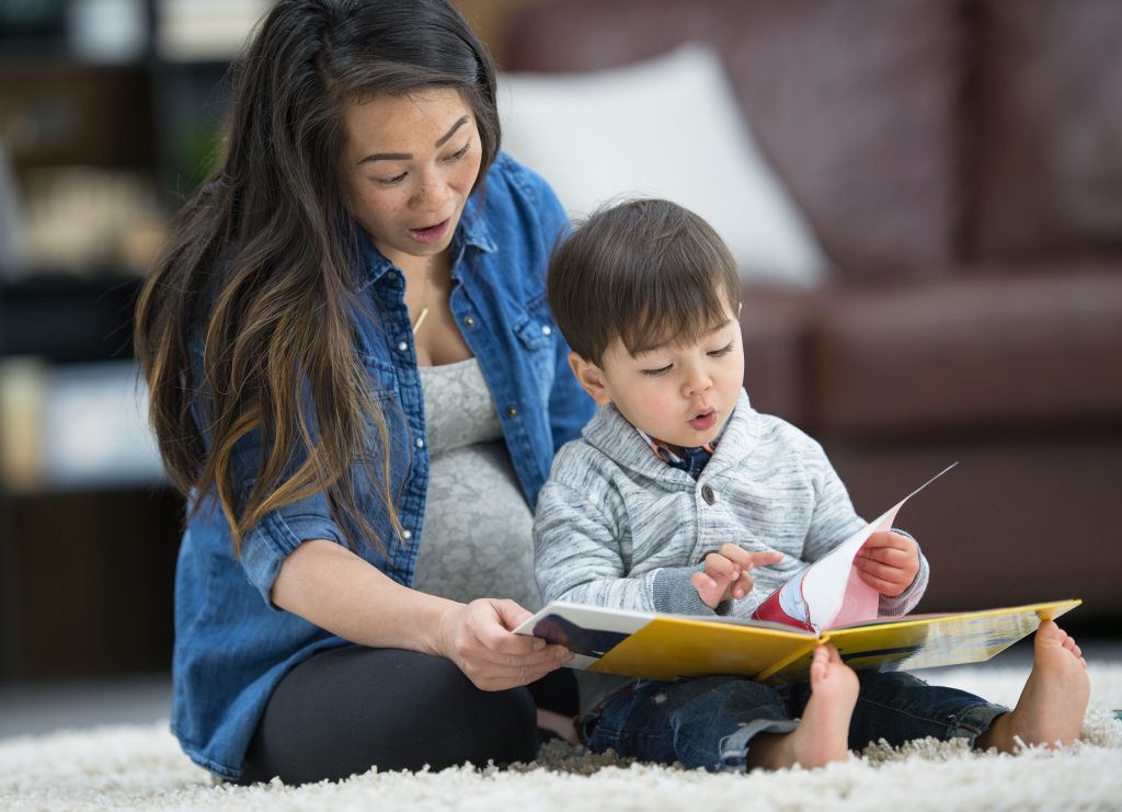 Mother reading to toddler sitting on floor
