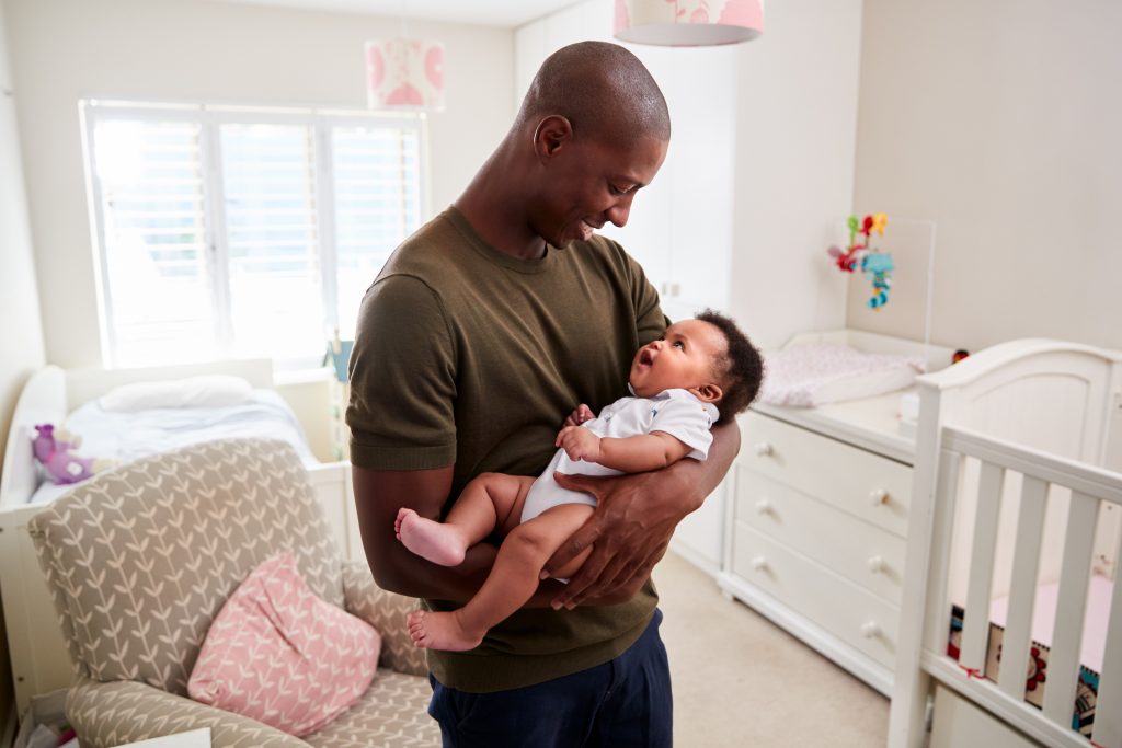 Father holding infant in arms and smiling down at infant. 