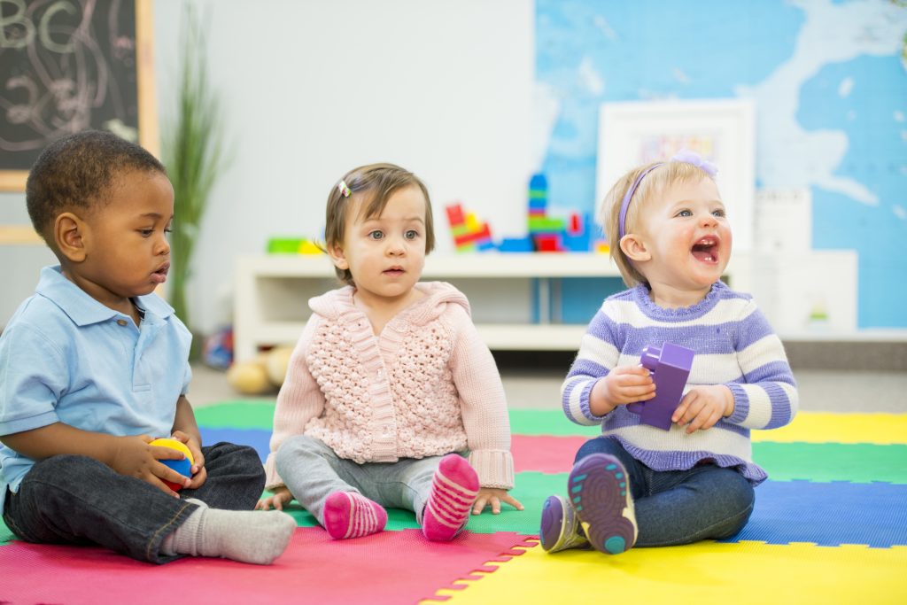 three toddlers sit together in Montessori classroom at circle time