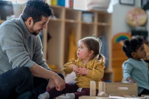 Montessori teacher sitting on work mat and speaking with toddler