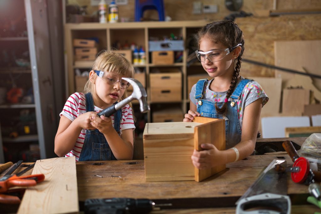 two elementary students hammering nails into a birdhouse