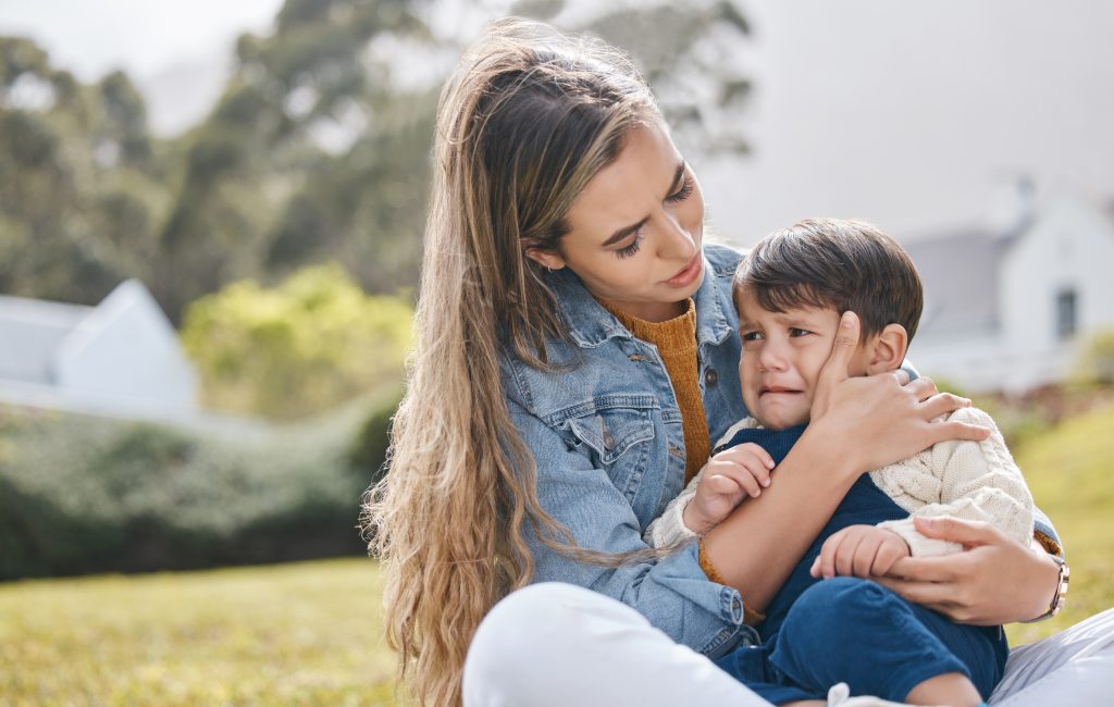 Toddler sitting on teacher's lap outside. Toddler is distressed and being comforted