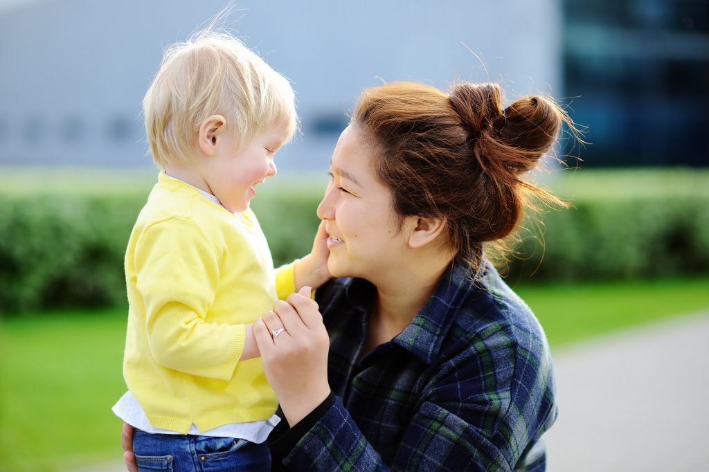 Toddler and caregiver sharing a comforting moment. Caregiver is kneeling in front of toddler, toddler's hand is on caregiver's face