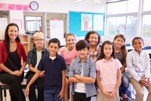 Group of elementary students and teacher in classroom, all facing camera