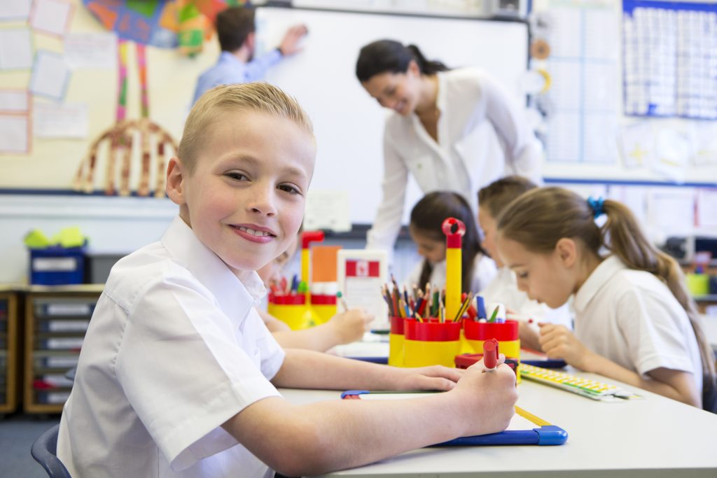 Montessori student working at table with other students, facing camera