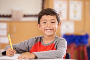 Elementary student writing in journal, smiling at camera