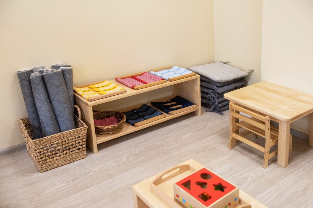 Montessori infant/toddler environment, low shelves with dressing frames, basked of rolled mats low tables and chairs