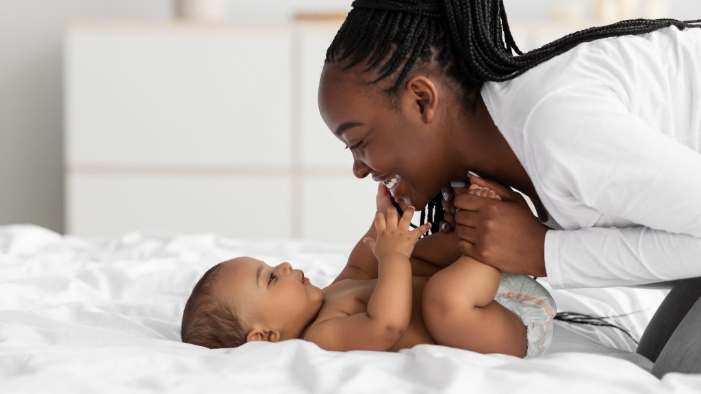 Infant lying on bed, mother leaning over them and smiling