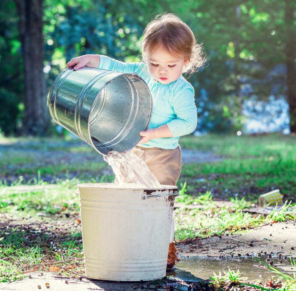 toddler pouring heavy water bucket into a larger bucket