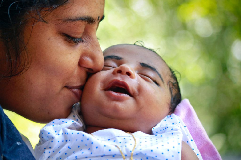 mother holding newborn baby and kissing cheek