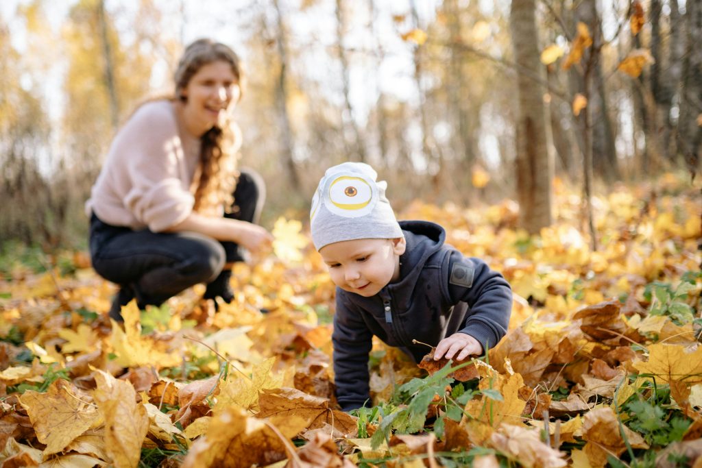 toddler playing in fall leaves mother smiling in background