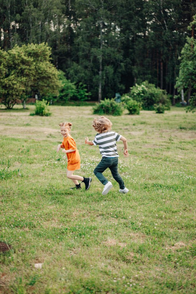 two children chasing each other in grass field