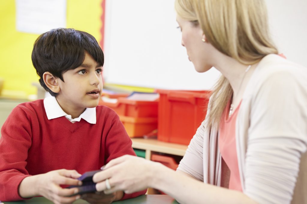 Teacher and elementary student sitting at table and having a discussion
